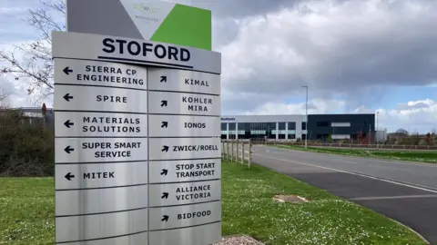 A large metal sign listing some of the companies which are trading at Worcester Six business park. The sign is on a grassy verge with big buildings visible in the distance.