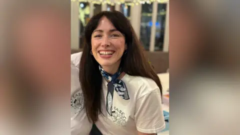 Emmy Porter Emmy Porter has dark brown hair, wears a t-shirt and a blue neck scarf and is smiling at the camera.