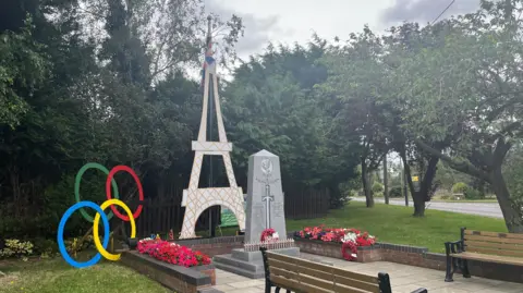 BBC A model of the Eiffel Tower and Olympic rings sit alongside a war memorial, with flower beds and benches in front