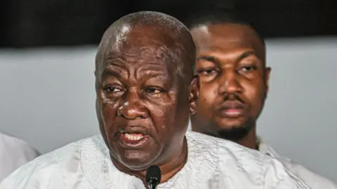 AFP Ghana's President-elect John Dramani Mahama in a white robe speaks into a microphone. A man's face appears behind him.