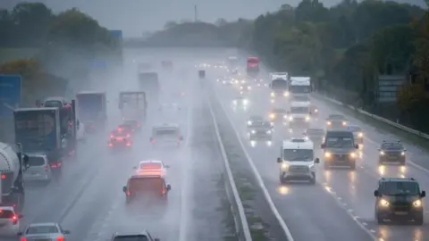 Ben Birchall/PA Wire A very wet M5 motorway viewed from a bridge above the carriageways, with substantial spray under very busy conditions as many cars, vans and lorries tackle the difficult conditions in poor visibility.