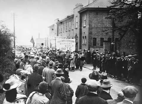 Getty Images A black and white image of people lining the streets of Crewe as a protest took place during the General Strike. Some are holding a banner 