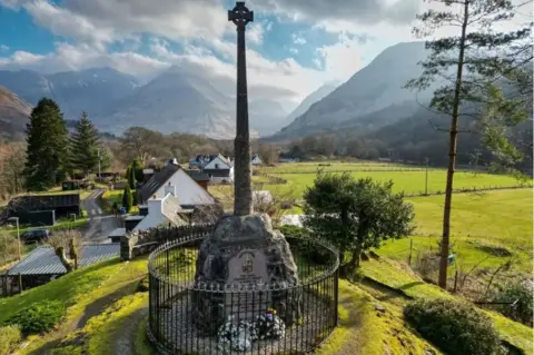 Getty Images The Glencoe massacre memorial - a Celtic cross mounted on a rock - stands in the village with imposing mountains in the distance.