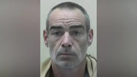 Northumbria Police Mugshot of Hogan. He has short greying hair and scruffy stubble.