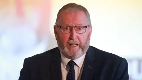 PA Media Headshot of Doug Beattie speaking. He is wearing a suit and tie. The background is out of focus.