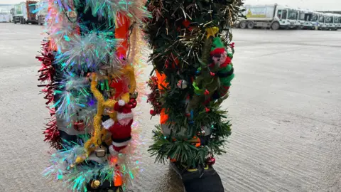 Tom Jackson/BBC Lenny Edward legs are covered in tinsel. There are knitted elves attached to the tinsel on his uniform which look as though they are climbing up his legs. 