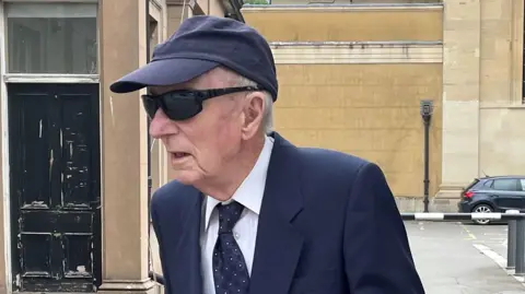  Peter Burrow in dark glasses, a dark blue cap and dark blue suit with a dark blue tie and white shirt pictured leaving court