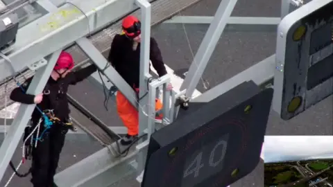 Essex Police A police officer works to remove a protestor from the gantry over junction 30 of the M25 in November 2022