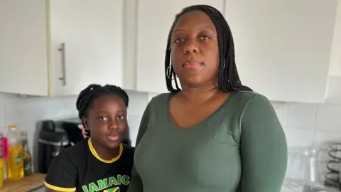 BBC A nine year old girl wearing a black print t-shirt stands beside her mother who is wearing a long sleeved green t-shirt