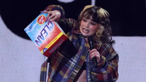 Reuters Singer Lola Young on stage singing - with a cleaning product used as a prop.