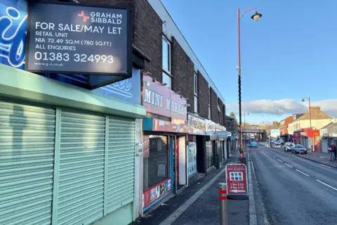 There is a green shuttered shop in the foreground. The street stretches into the distance.