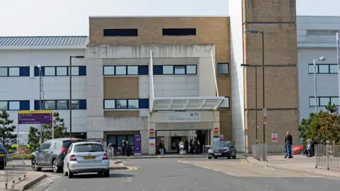 The exterior of Edinburgh Royal Infirmary, a large white and brick-coloured building, with cars parked outside 