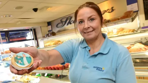 Pacemaker Press A woman with brown hair tied back is standing in a bakery holding a German biscuit with Rory McIlroy's picture on it. Behind her is shelves of baked goods.