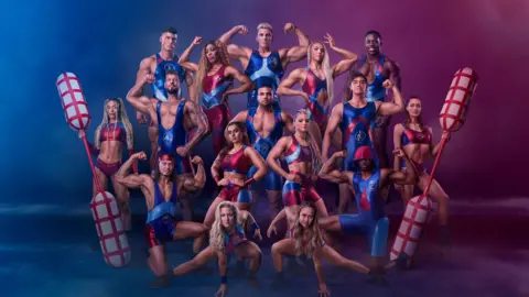 Nick Eagle/BBC/Hungry Bear The elite athletes on the TV show Gladiators. They are all dressed in lycra outfits and stood against an artistic red and blue backdrop. The figures on the end are holding large oars.