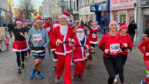 Image of people in Santa outfits running through a high-street. 