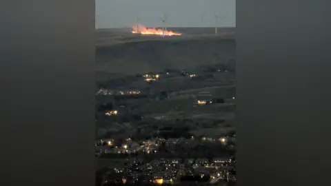 Carl Greenhalgh Fire on moorland near wind turbines.