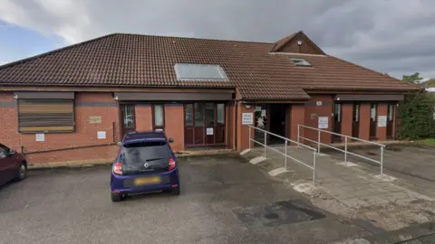 Google Billinge Medical Practice is a red brick single storey building, with a blue car parked outside the front.