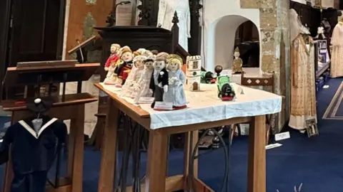 Carol Clayton A knitted centrepiece which depicts several couples who are wearing different wedding garments. The feature is placed on a table as part of a wedding-themed exhibition at St Andrew's Church.