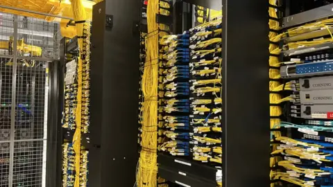 A general view picture of a data centre's infrastructure with yellow data cables trailing from many ports.