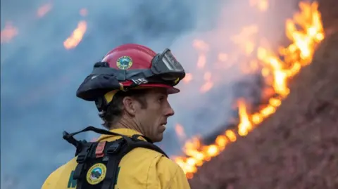 A firefighter watches as the Palisades Fire, one of simultaneous blazes that have ripped across Los Angeles County, burns at the Mandeville Canyon, a neighborhood of Los Angeles, California, U.S. January 11, 2025.