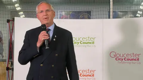 BBC A man wearing a navy blue suit holding a microphone