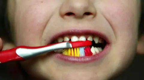 Close up of a young child's mouth as they brush their teeth with a red and white toothbrush