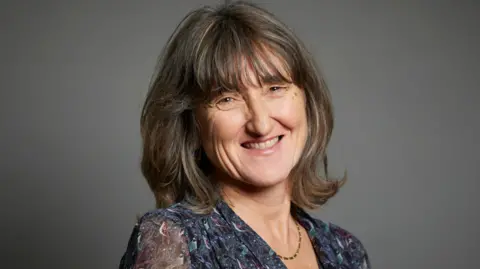 Roger Harris Photography/UK Parliament Baroness Kidron is smiling in a parliament portatrait. She has brown hair and is wearing a navy blouse. 