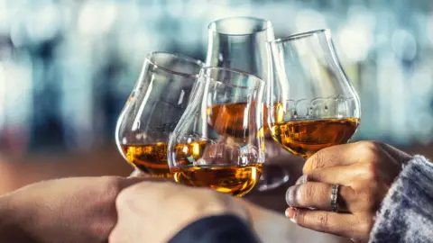 Several hands clinking small, balloon whiskey tasting glasses with liquor inside them