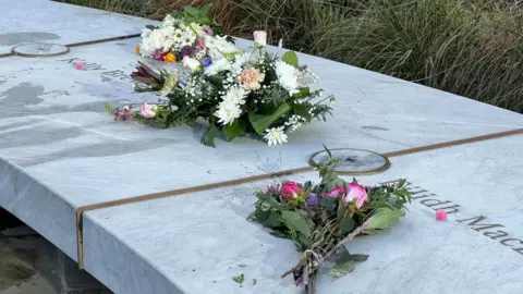 Two bunches of flowers on a marble bench with two names inscribed into it. 