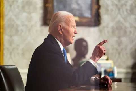 Demetrius Freeman/The Washington Post/Getty Images Presiden AS Joe Biden menunjukkan sosoknya saat menyampaikan pidato perpisahannya kepada AS dari mejanya di Ruang Oval Gedung Putih