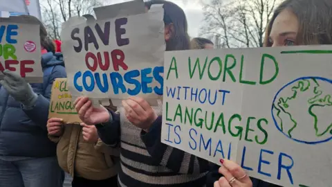 People holding up homemade placards which say "save our courses" and "a world without languages is smaller"