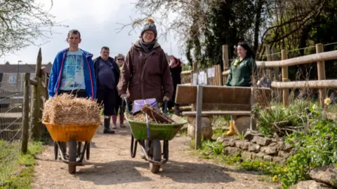Bath City Farm A man and woman walking with wheelbarrows in farm with people in the background.