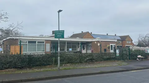 Alice Cunningham/BBC A general view of Blossom preschool in Colchester. The school is single storey and is surrounded by a large gate. A playground sits directly outside the school's entrance.