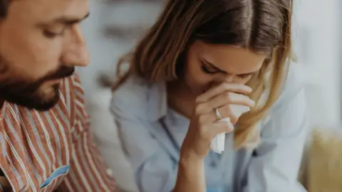 A close up stock photo shows an emotional couple crying at home.