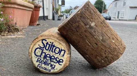 Natalie Malcolm/BBC Two logs are placed on a road. One of them has the words "Stilton Cheese Rolling Festival" printed on it