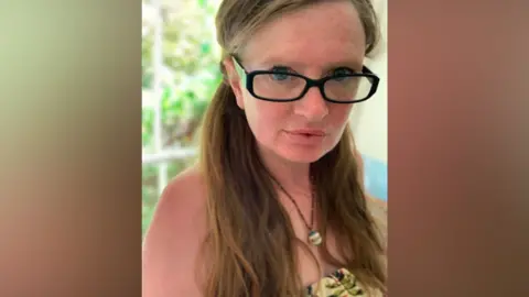 Rachel Kingsbrook Rachel Kingsbrook with long red hair and glasses is wearing a strapless top and a long necklace, with a bead attached to the end. 