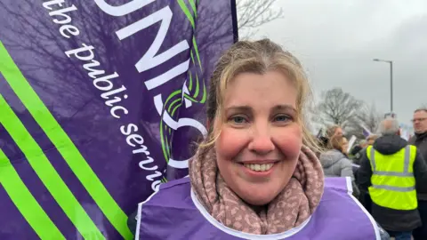A healthcare worker on the picket line with a Unison flag behind her