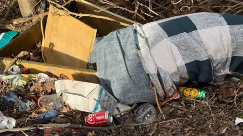 A duvet and empty cans of cola and beer litter undergrowth