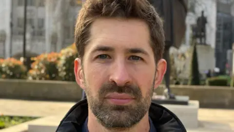 Andrew Sinclair/BBC George Gabriel, co-founder of The Dad Shift, standing outside Parliament during the lobby of MPs