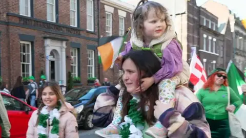 A woman carries over her shoulder a little girl who holds a tricolour flag .