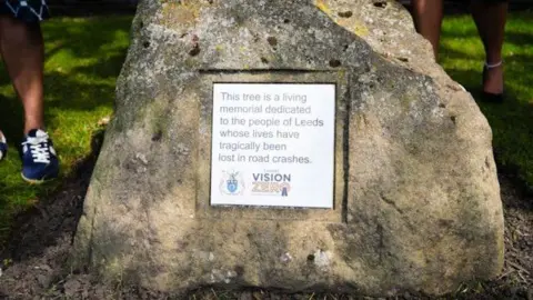 West Yorkshire Combined Authority A white plaque on a rock, with the message: "This tree is a living memorial to the people of Leeds whose lives have tragically been lost in road crashes."