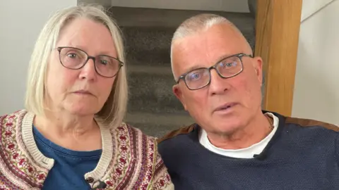 Denise and her husband Colin sitting looking at the camera