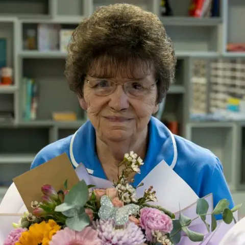 NHS Humber Health Partnership A head and shoulders shot of Cath Lyon, who was short brown hair, wearing a nurse uniform and holding a bouquet of flowers.