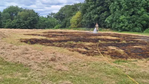 Derbyshire Fire and Rescue Service A firefighter hosing a patch of burnt grass