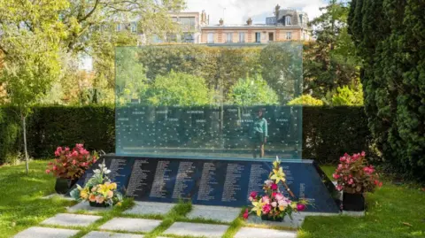 Universal Images Group via Getty Images It is a large, translucent board with 228 swallows and the words "in memory" in 20 languages inscribed above a list of the names of the victims.
