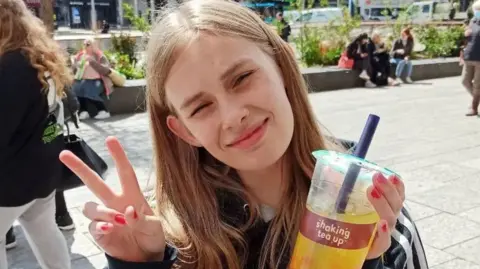 Rhianan holding up a cup of bubble tea and giving a peace sign to the camera.