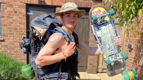 Sam Allison stands with a backpack and a skateboard