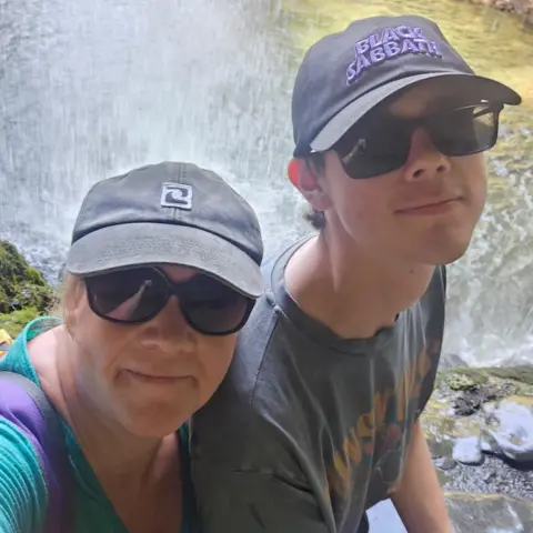 Ruth Bint A mother and son wearing baseball caps and sunglasses and standing in front of a waterfall
