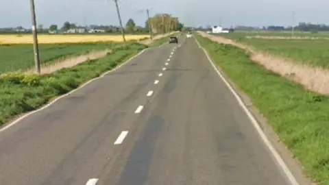 A Google picture of a flat road and landscape, with green fields on both sides of the road.
