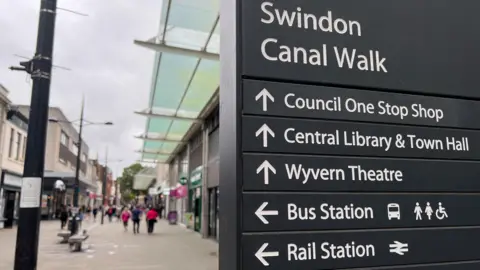 View of a sign on Canal Walk in Swindon with the town centre behind it